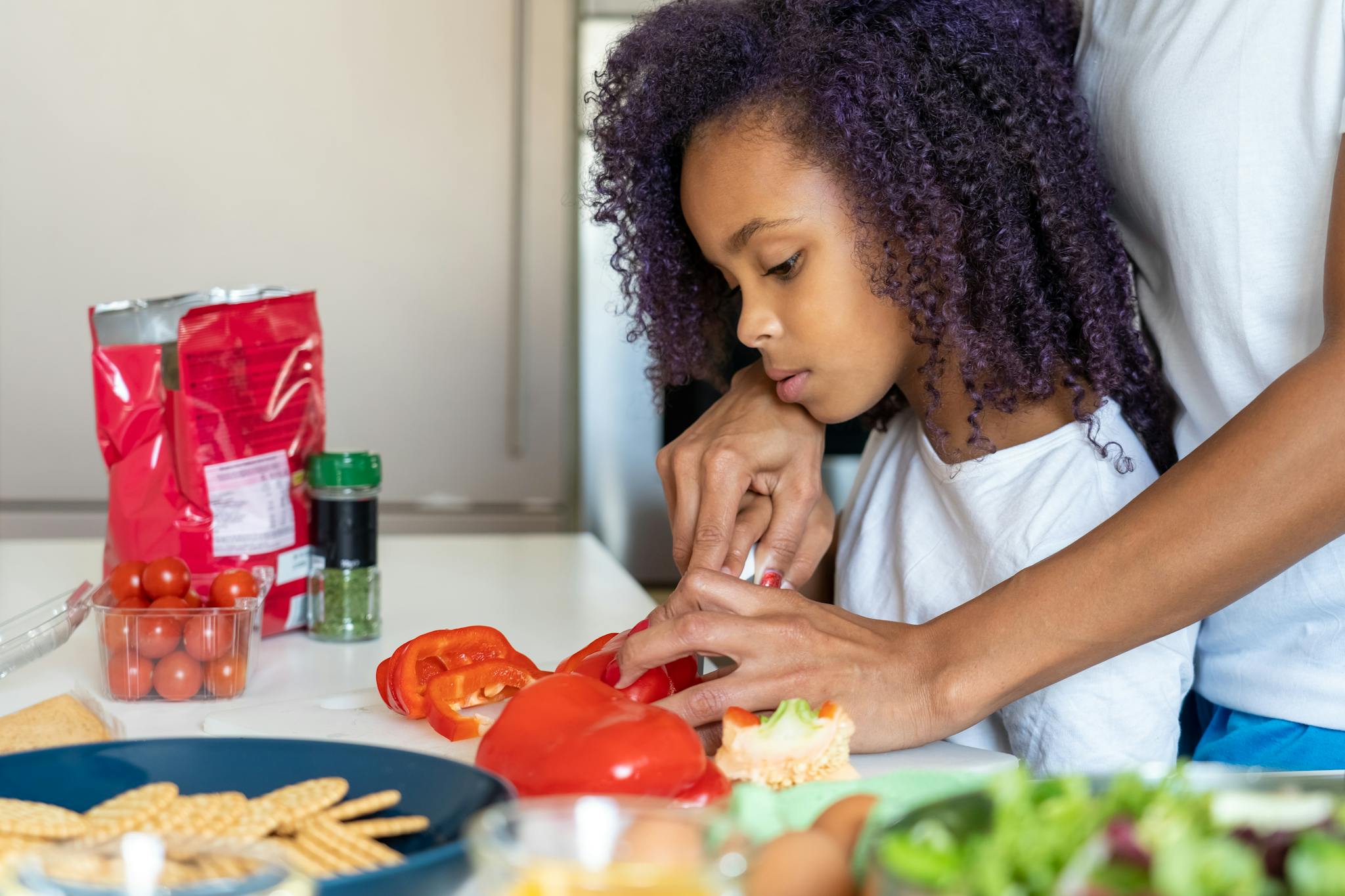 A mother helps her daughter slice bell peppers in a home kitchen.
