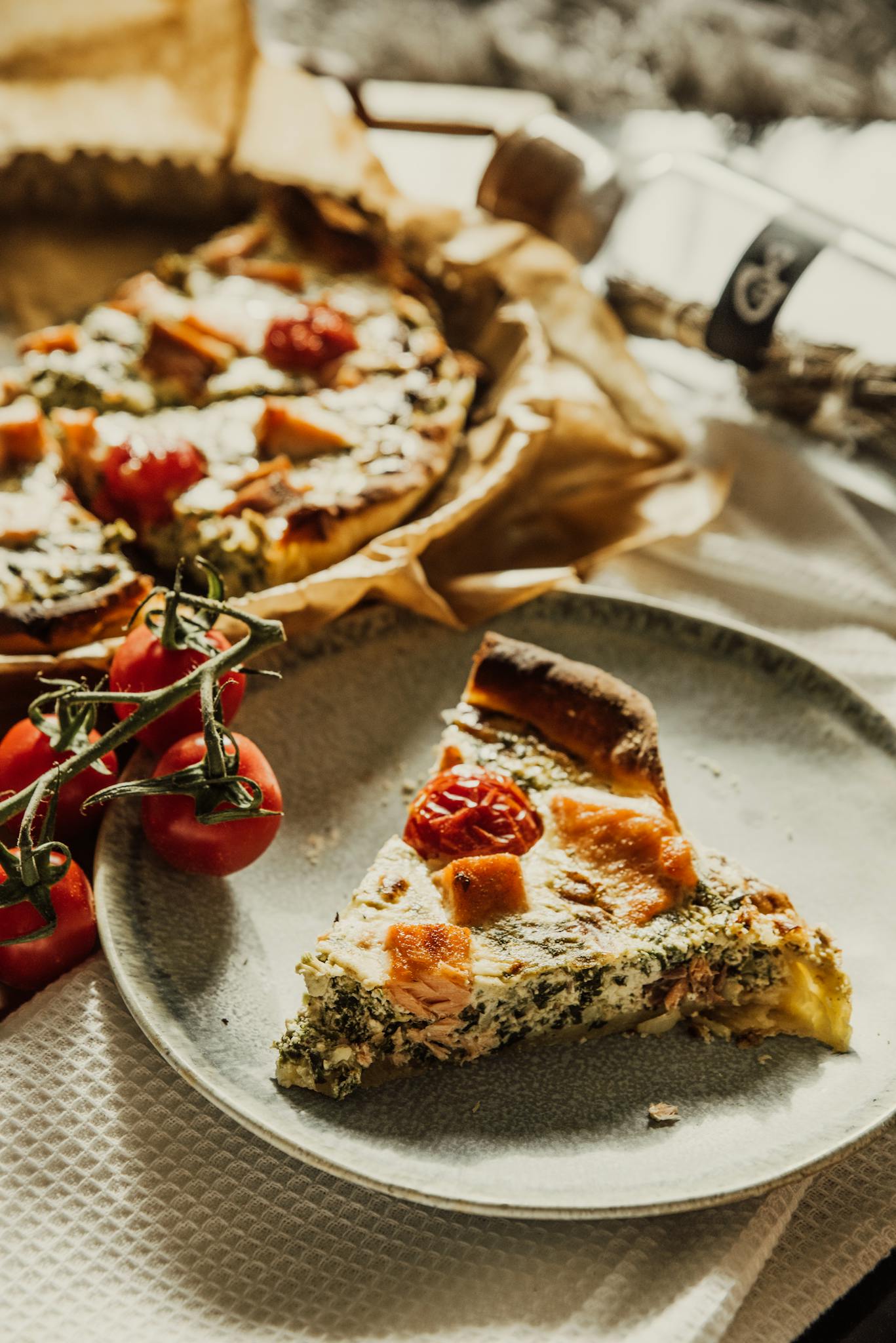 Close-up of appetizing spinach quiche garnished with tomatoes and cheese on a plate.